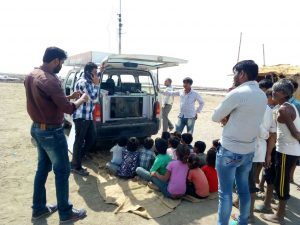 Children-and-men-gather-to-watch-videos-on-health-and-education-being-screened-from-the-van-300×225